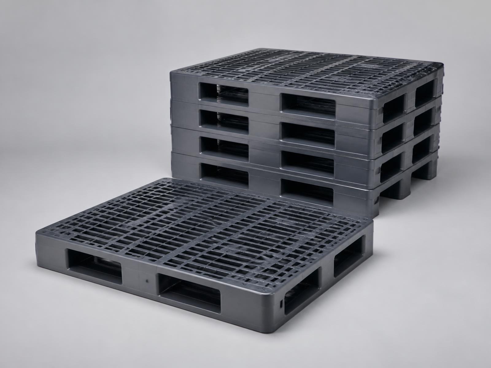 Heavy duty dark grey plastic pallets, one in front of a stack, with ribbed moulded decks
